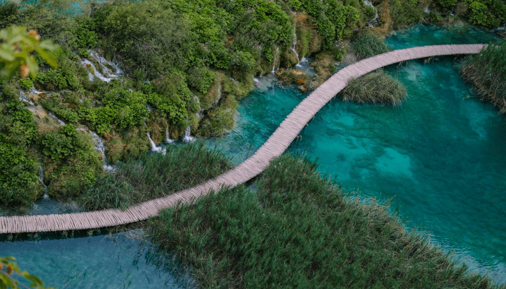 Krka National Park vs. Plitvice Lakes: The Honest Comparison for 2026 3 Tourists walking on wooden boardwalk trails over turquoise water at Plitvice Lakes National Park